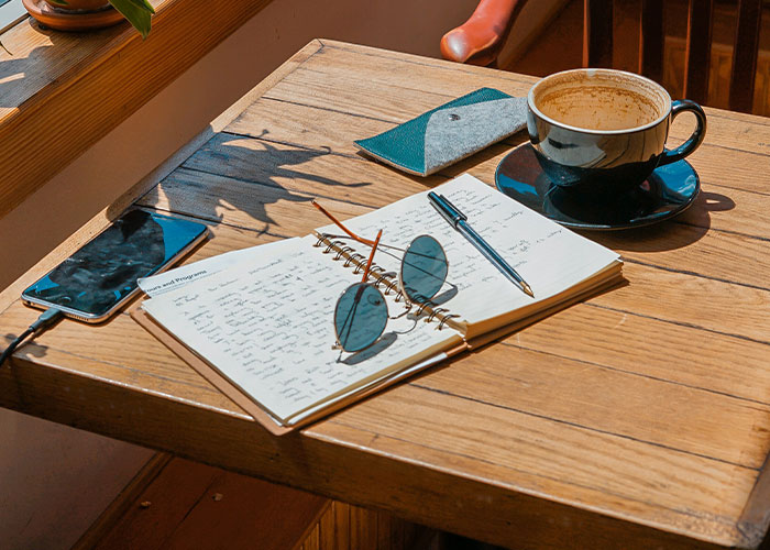 Notebook with writing, sunglasses, and a coffee cup on a wooden table, evoking a whimsical life atmosphere.