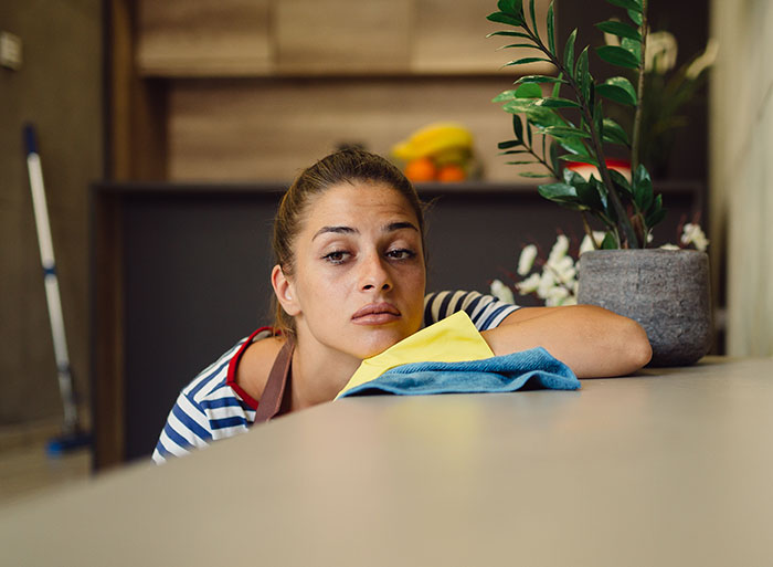 Woman looking tired while cleaning, embodying frustration over houseguests treating her home like a hotel.