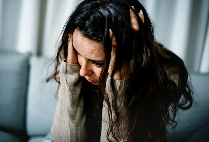 Stressed woman with long hair holding her head, concerned about a cruise during DIL's early birth.