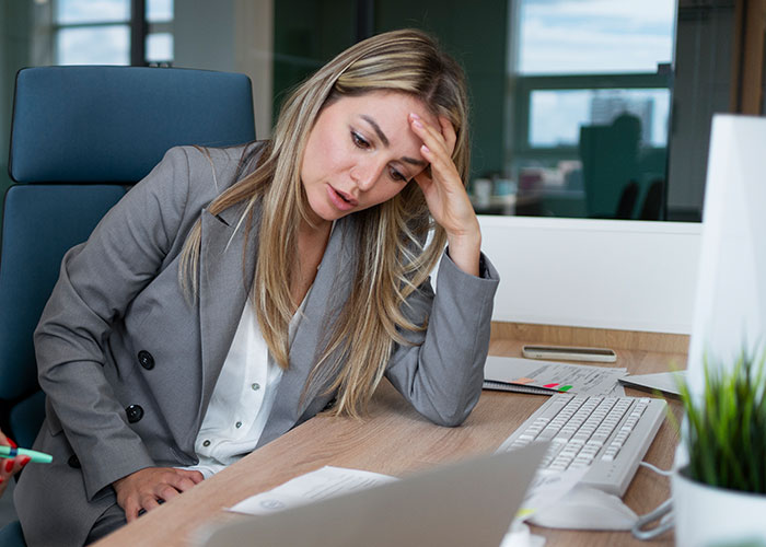 Stressed woman at desk in office, dealing with workplace issues.
