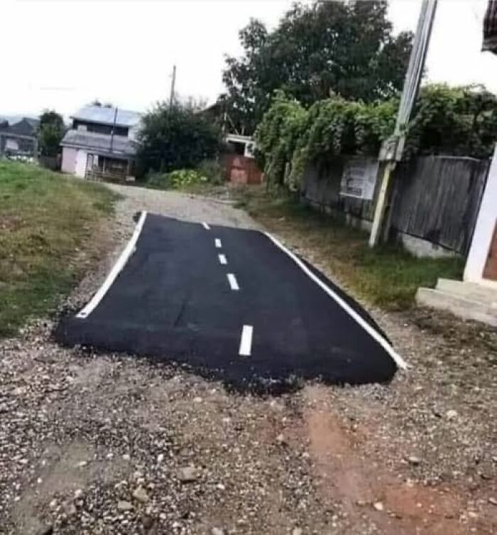 Weird image of a short random asphalt road segment in a rural area, ending abruptly on gravel.