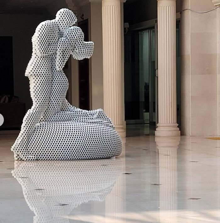 Metal pipe sculpture depicting two figures embracing in an elegant indoor setting.