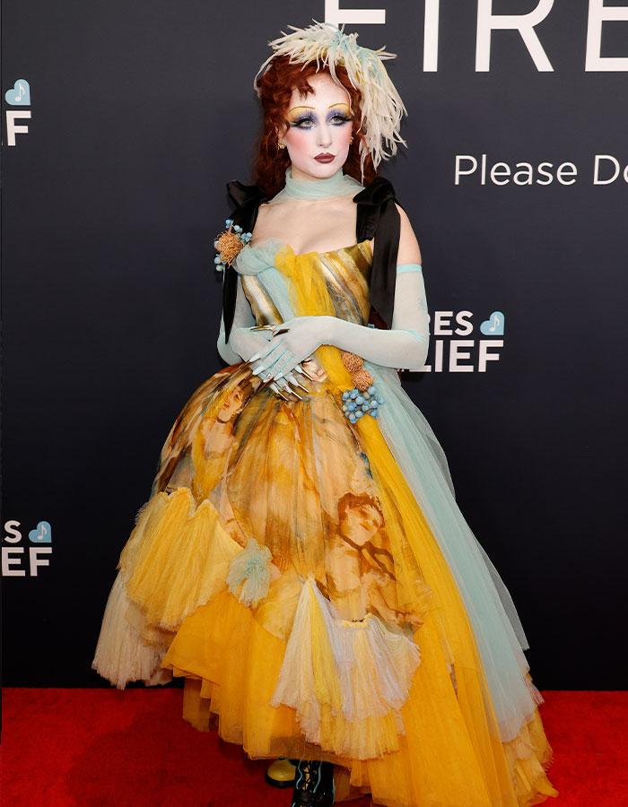 Red carpet fashion from the 2025 Grammys: person in a colorful, artistic gown with dramatic makeup and feathered headpiece.