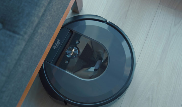 Robot vacuum cleaner navigating under a couch on a wooden floor.