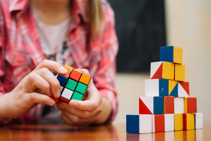 Individual solving a Rubik's Cube with a stack of colorful blocks nearby.