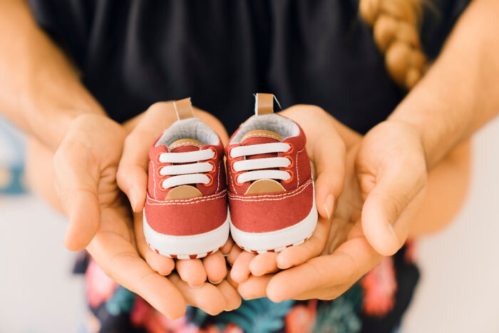 Adult hands holding small red baby shoes, symbolizing childhood experiences and memories from being raised.
