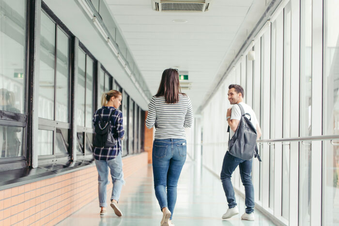 People walking down a hallway, possibly discussing rules implemented due to one individual.