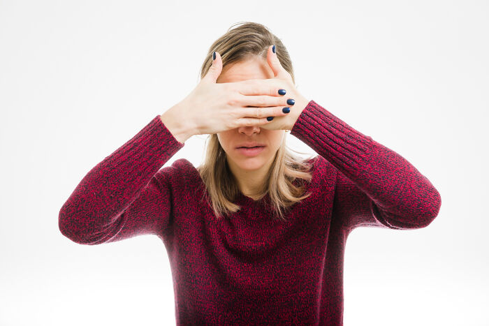 Woman in a red sweater covering her eyes, illustrating American norms surprising to foreigners.