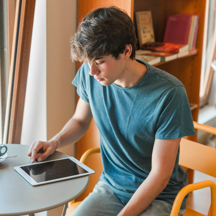 Person using a tablet at a table with bookshelves behind, illustrating individual influence on new rules.