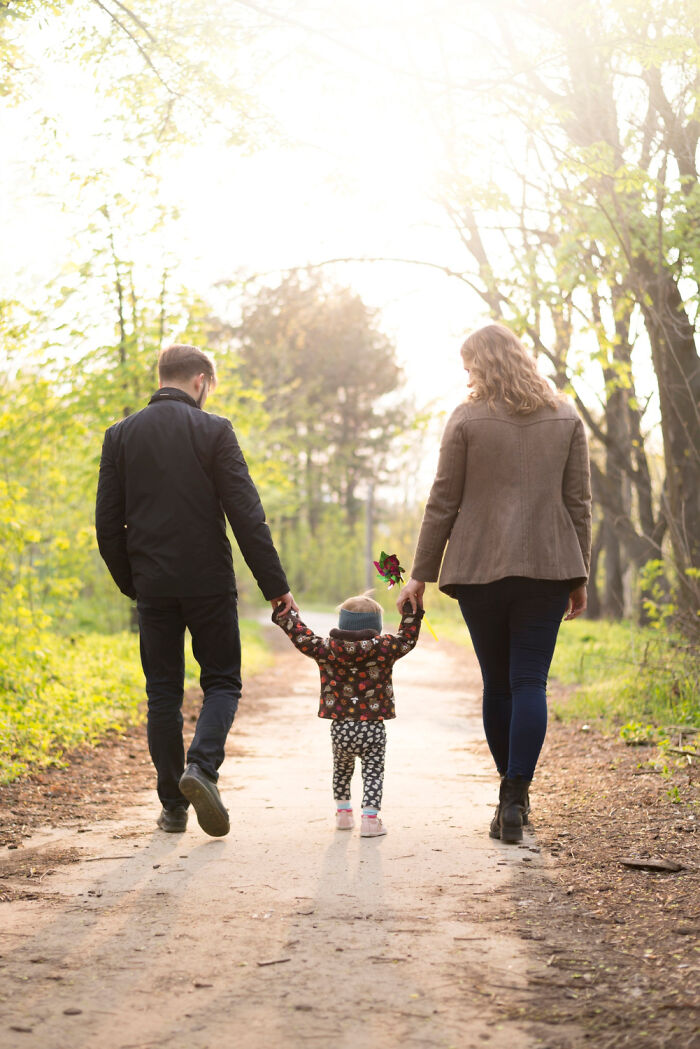 Family walking on a forest path holding hands during a sunny day, highlighting childhood experiences and common upbringing.