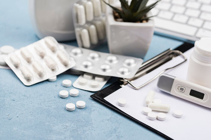 White pills and capsules in blister packs with a thermometer and a clipboard on a blue surface, illustrating common experiences.