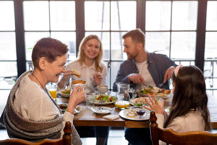 Family enjoying a meal together, sharing experiences around a table with coffee and plates of food in a cozy setting.