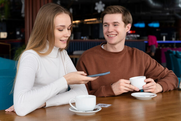 Two people having coffee together, one using her smartphone.
