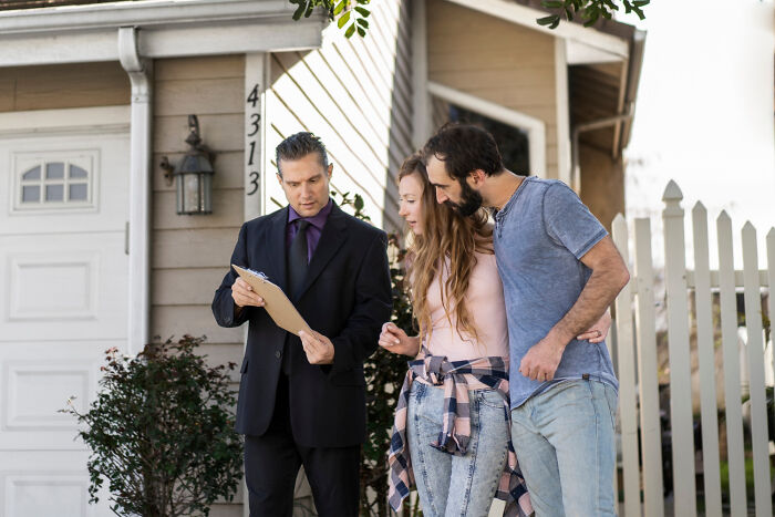 A couple reviewing paperwork with a real estate agent outside an American house.