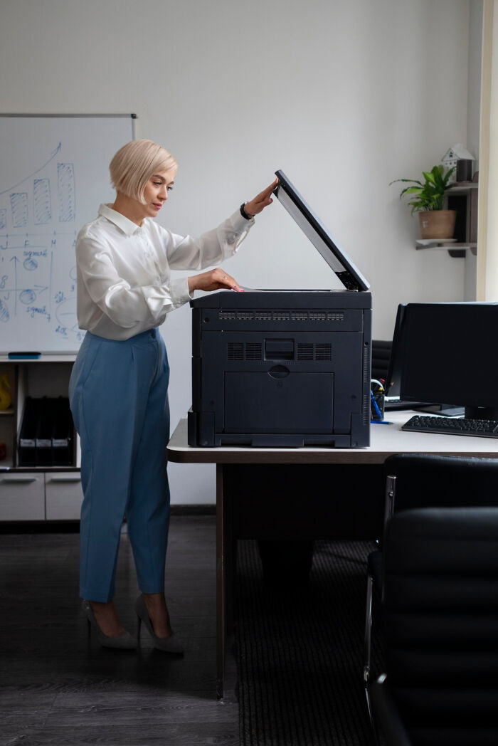Woman in office using a copier, in a professional setting, emphasizing a common workplace scenario.
