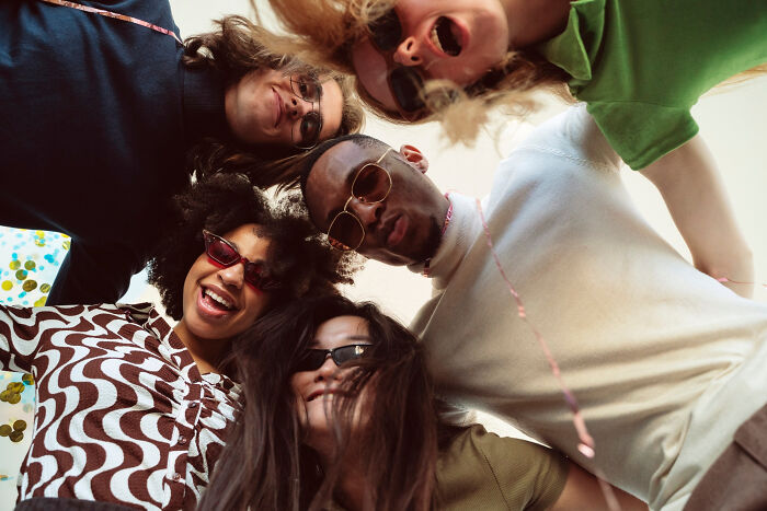 Group of friends smiling and looking down at the camera, embracing life's harsh realities with joy.
