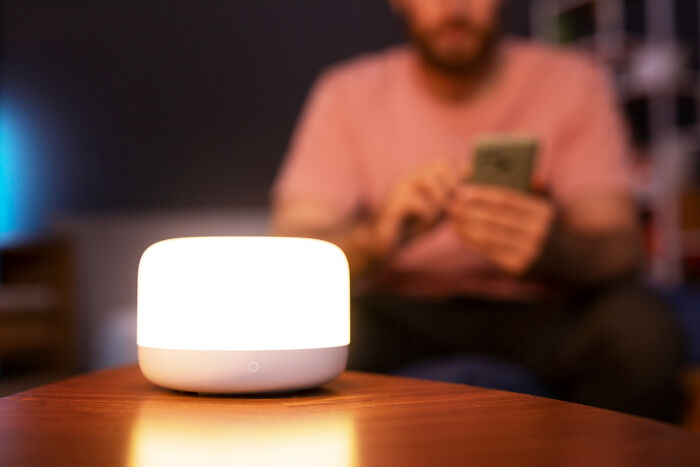 A soothing travel essential light glows on a table while a person in the background uses a smartphone.