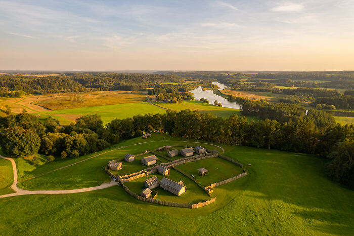 Aerial view of Lithuania showcasing a lush landscape with historical wooden structures surrounded by greenery.