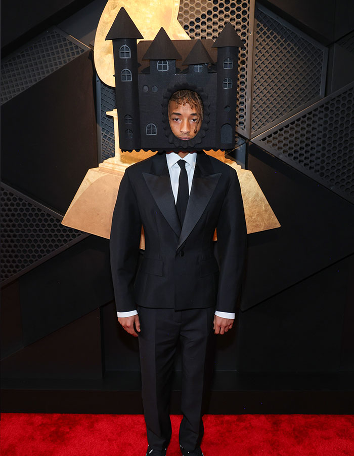 Person wearing a castle-shaped headpiece and black suit on the red carpet at the 2025 Grammys.