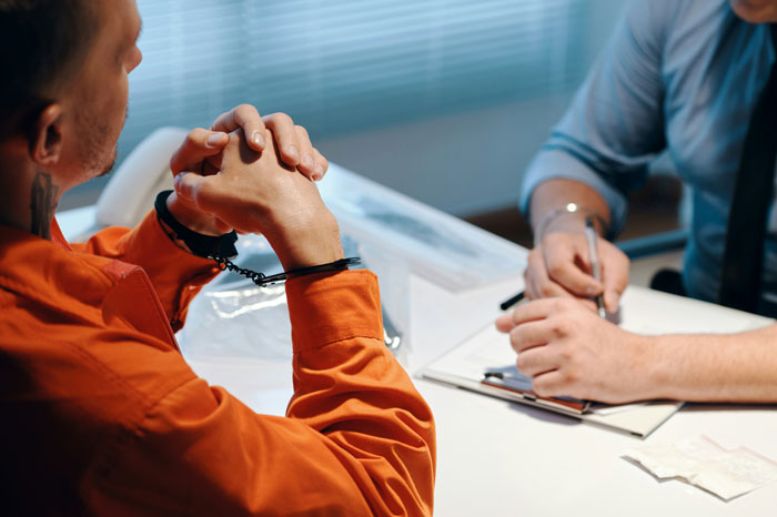 Man in handcuffs in orange clothing being questioned, hinting at uncovering background information.