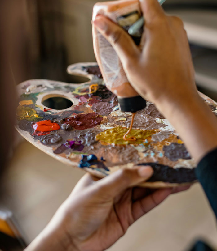 A student artist squeezes paint onto a palette, preparing for a colorful and potentially hilarious painting session.