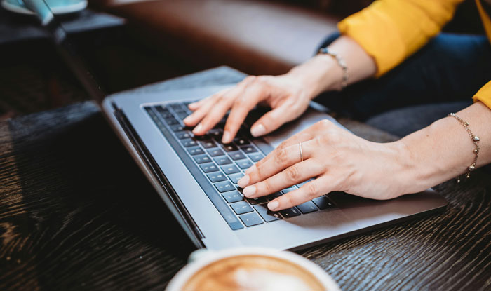 Hands typing on a laptop keyboard, researching a man's background.