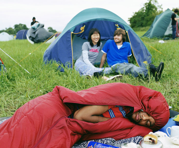 People camping outdoors, one sleeping in a red sleeping bag, highlighting differences in perception of camping.