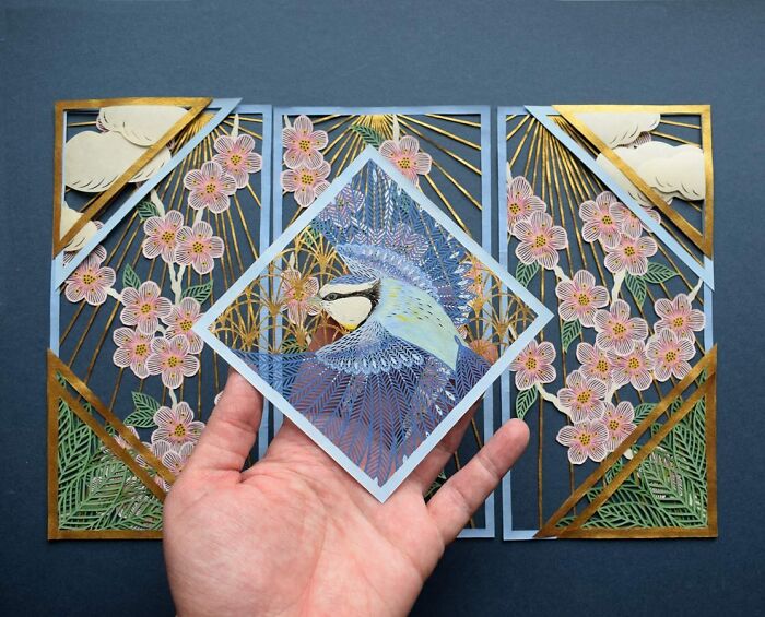 Hand holding a nature-inspired intricate paper art design with floral and bird motifs.