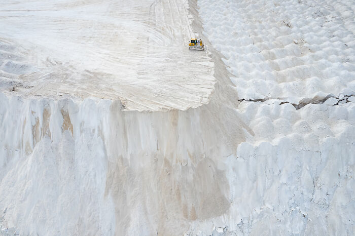 Bird’s-eye view of white cliffs in Lithuania with a bulldozer on top, highlighting the landscape's unique features.