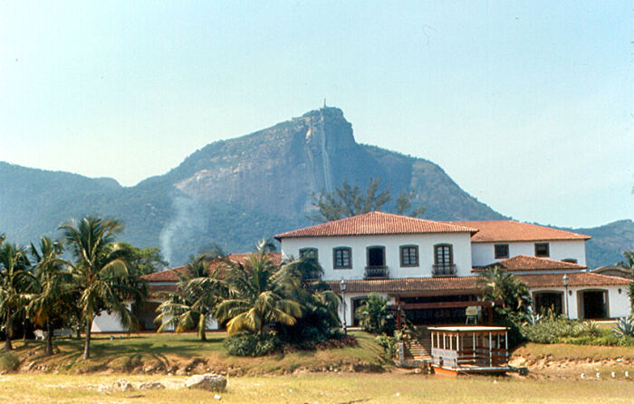 Retro Brazilian scene with a white colonial house, palm trees, and a mountain backdrop.
