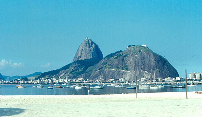 Retro Brazilian beach scene with Sugarloaf Mountain in the background, boats on the water, and clear blue skies.