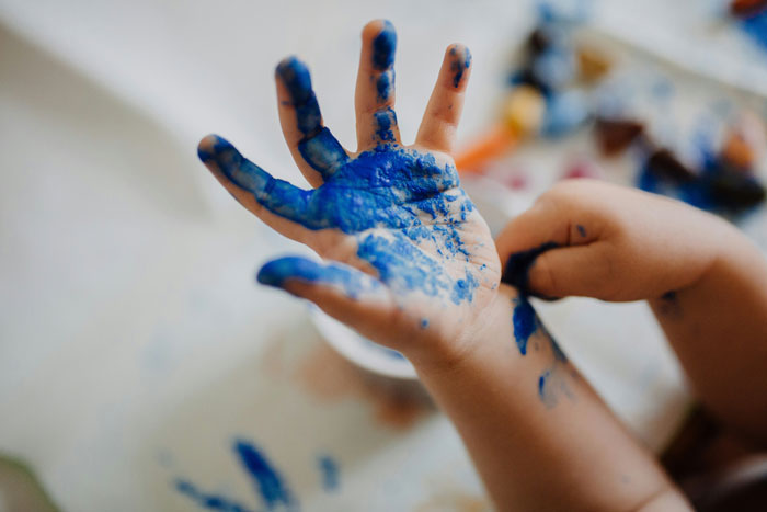 Child's hand covered in blue paint, illustrating disparity in perceptions of creativity across socioeconomic backgrounds.