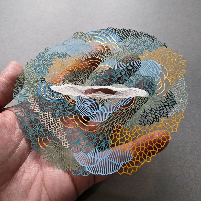 Intricate paper art design inspired by nature held in a hand, showcasing delicate patterns and diverse colors.