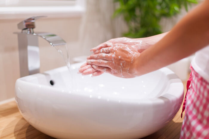 Person washing hands in a white sink with soap, focusing on hygiene habits to avoid stinky situations.