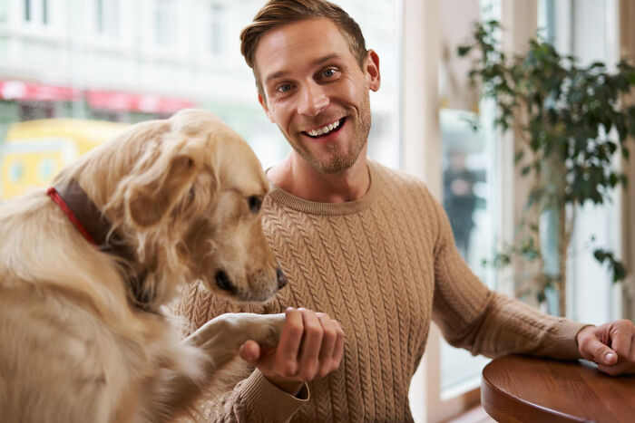 Man smiling, sitting indoors with a dog, wearing a tan sweater, highlighted in a discussion about dumbest things people have said.