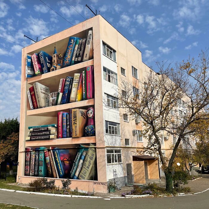Hyperrealistic mural by Jan Is De Man on a building wall, featuring a 3D illusion of a bookshelf filled with various books.