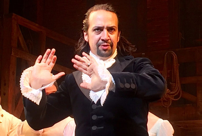 A performer in historical attire on stage, gesturing expressively.