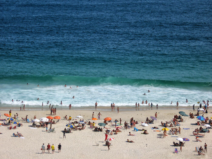 Retro Brazilian beach scene with people enjoying the sun and sand, colorful umbrellas scattered on the shore.