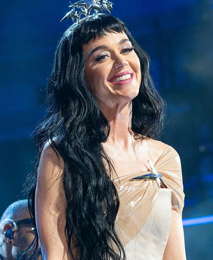 Smiling woman with long black hair and metallic outfit on stage, relating to discussion on singers.