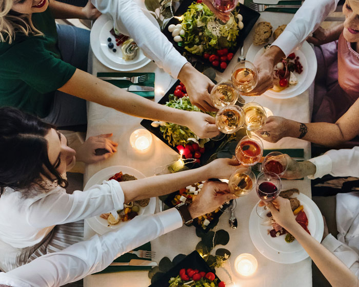 People toasting at a festive dinner, surrounded by food and candles, in a lively gathering atmosphere.