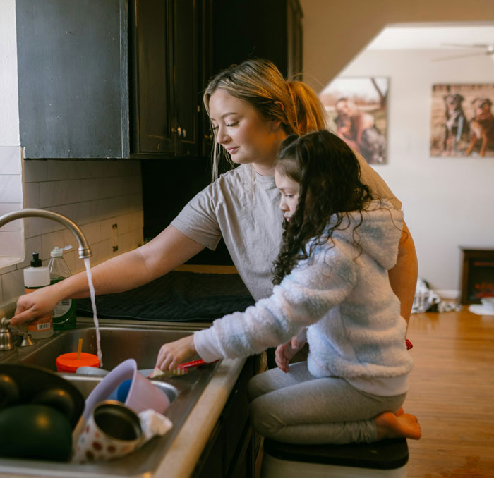 A woman and a child washing dishes together in a kitchen.