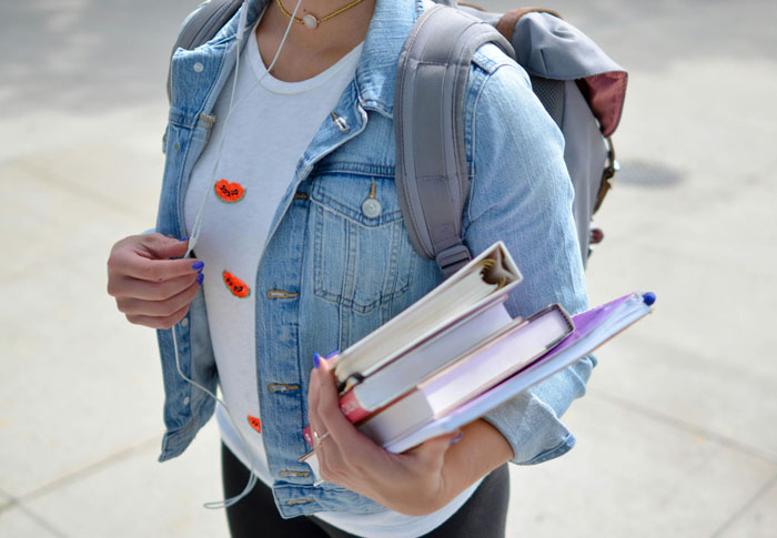 Person carrying books and wearing a denim jacket, suggests rich people might overlook common lifestyle needs.