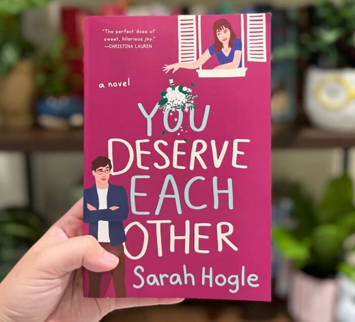 Romantic book cover: "You Deserve Each Other" by Sarah Hogle, held in hand, with illustrated couple.