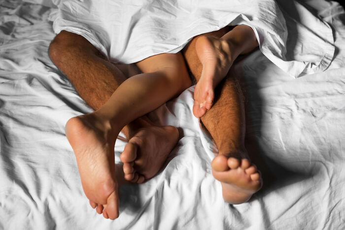 Two people's legs intertwined under white sheets, conveying an intimate moment.