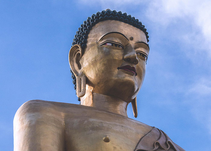 A large, serene Buddha statue set against a clear blue sky, embodying a delightfully wholesome presence.