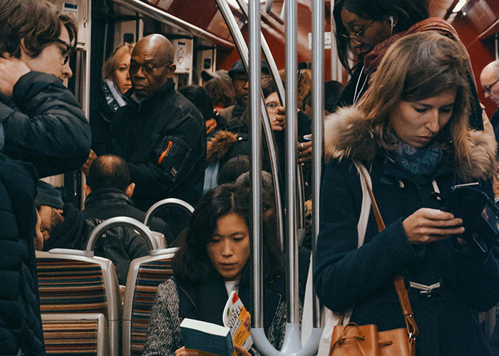 People on a crowded European train reading books and using phones during a commute.