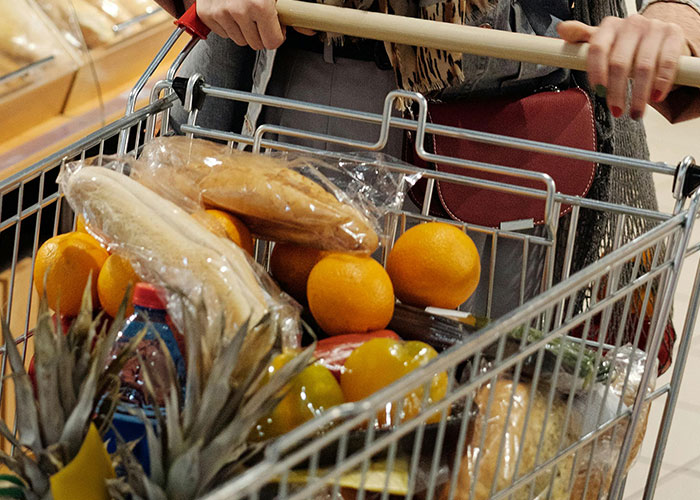 A person pushes a shopping cart filled with groceries, highlighting challenges of being overweight.