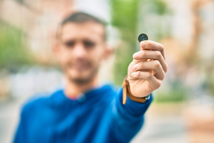 Man in blue hoodie holding a coin close to the camera, illustrating experiences people were raised to think were common.