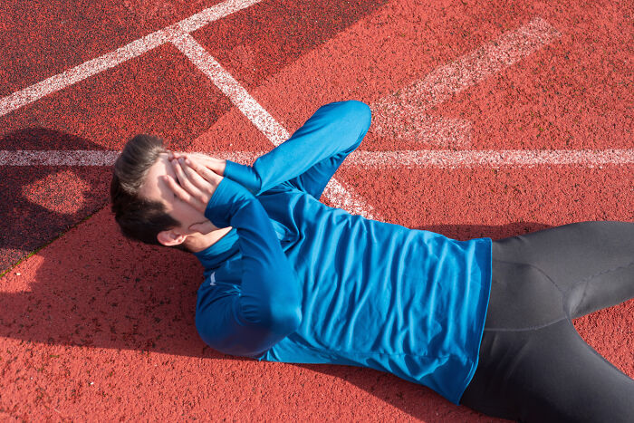 Person lying on a track field, covering face with hands, illustrating harsh realities about life.