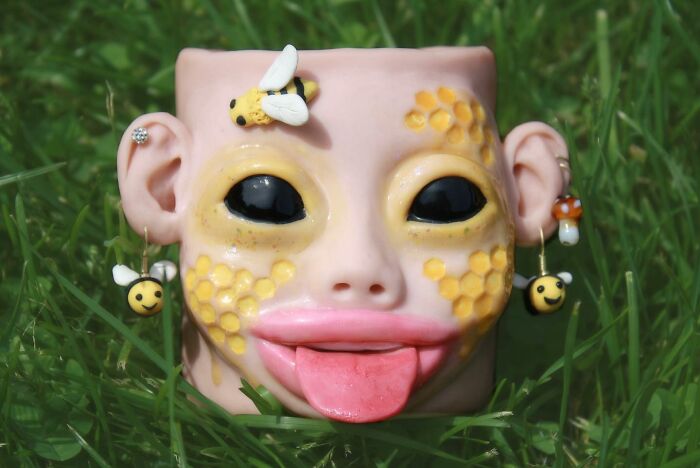 Unique creepy handmade craft depicting a face with bee decorations on grass.